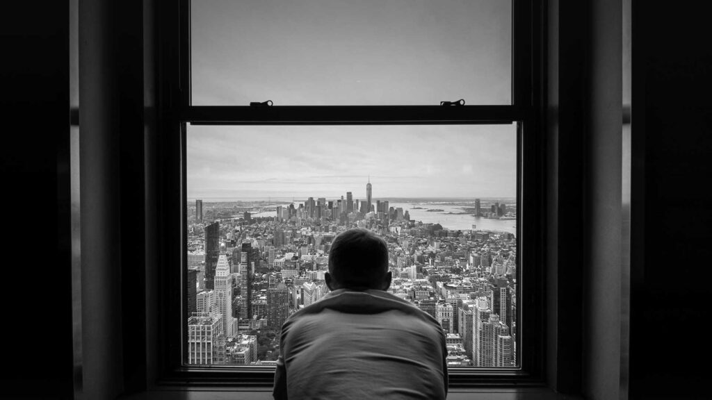 man-standing-by-window-looking-over-a-city